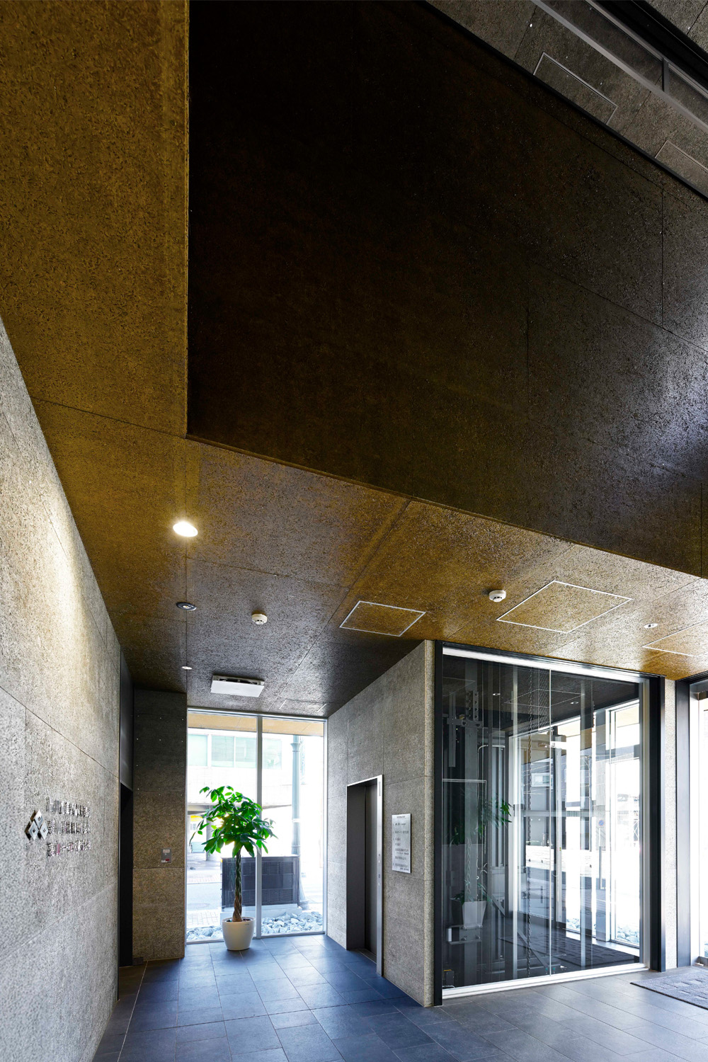 吹き抜けによる開放感のある1階エントランス。壁面の仕上げには、快適性、安全性、省エネ性などの機能を備えた木毛板（もくもうばん）を採用。メカニカルな昇降機と調和し、モダンな雰囲気を生み出している（エントランス：1階）